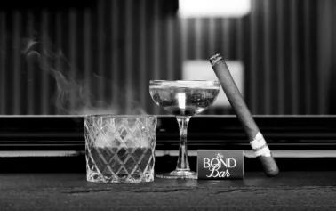 Black and white still life of a crafted cocktail, cigar, and glassware representing luxury mobile cigar and cocktail entertaining