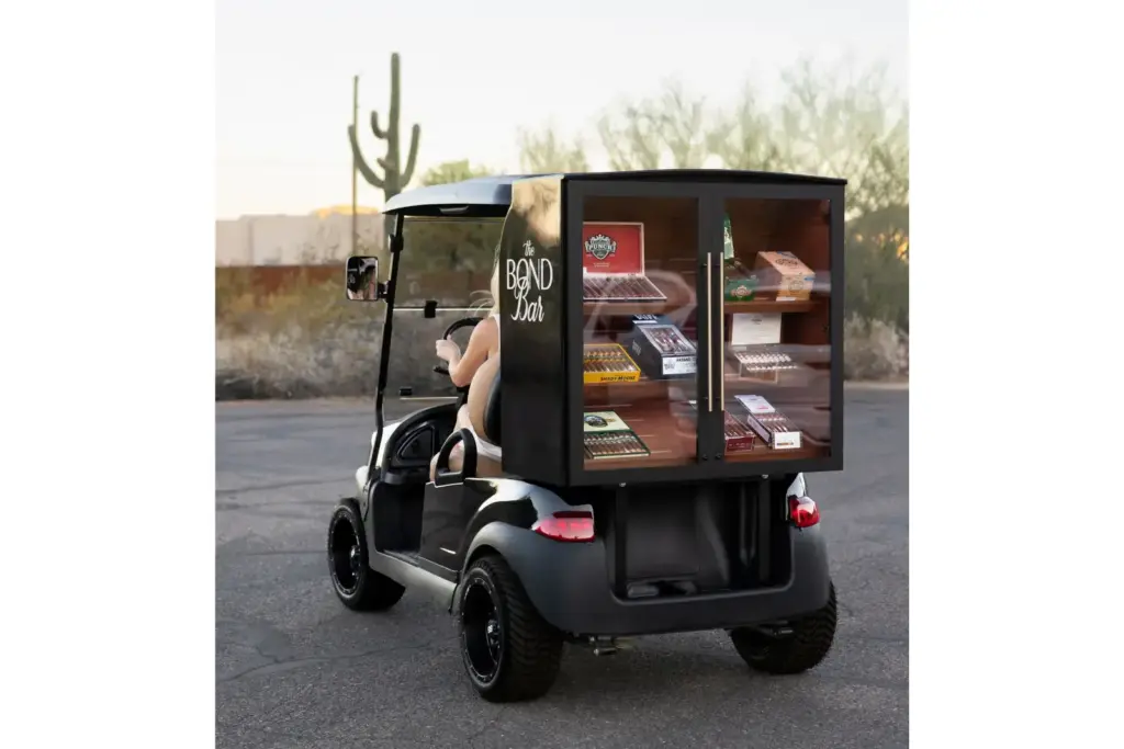 Black golf-cart with a glass-fronted cabinet on the back displaying cigars, labeled The Bond Bar