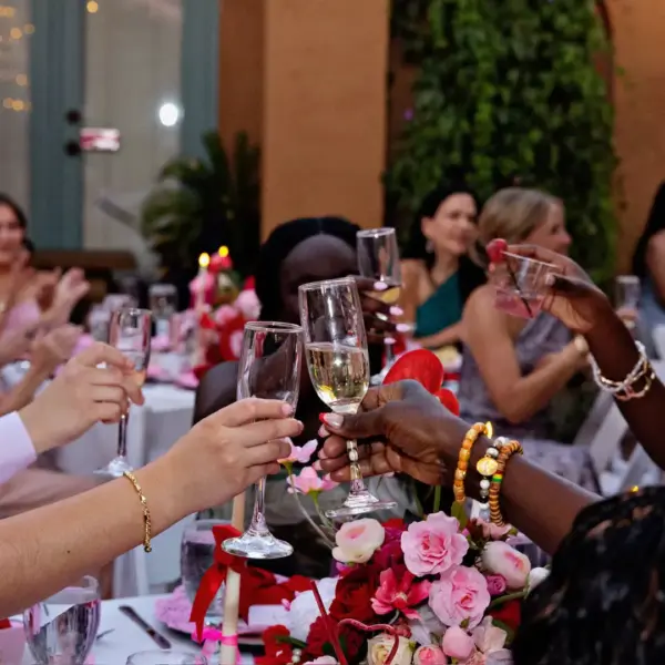 Group of people at a celebration toasting with champagne flutes over a table with pink flowers and candles.